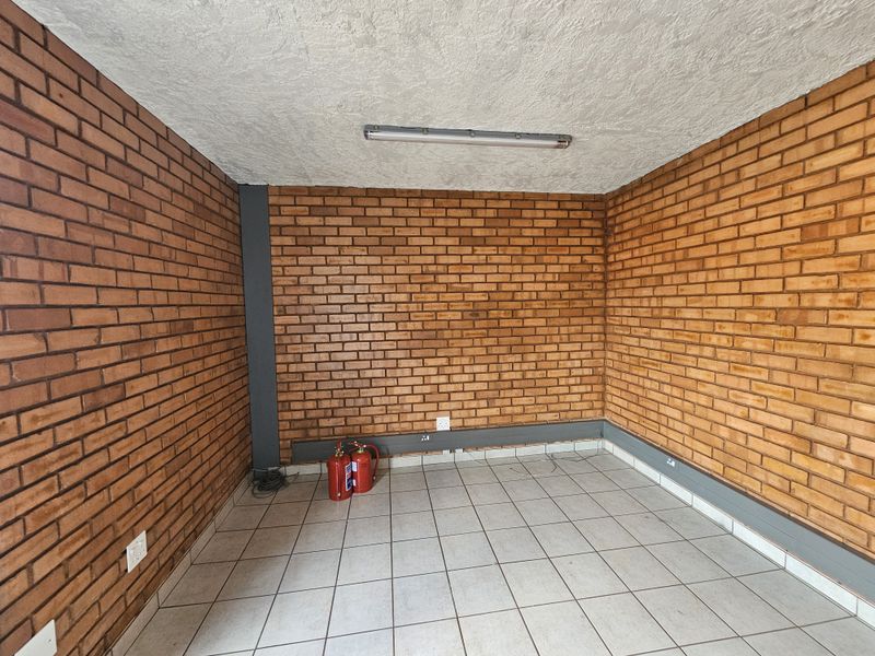 An empty industrial office space featuring exposed red brick walls, tiled flooring, and a functional fluorescent ceiling light fixture.