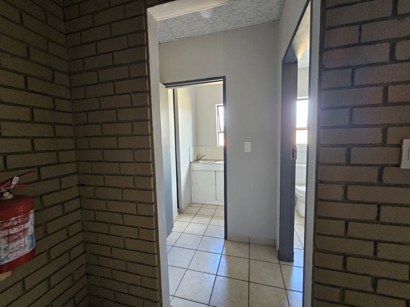 A view from a brick-walled hallway leading into a small kitchenette and a separate bathroom area with tiled flooring.