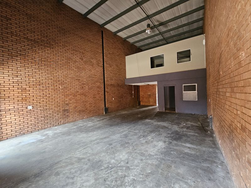 Spacious industrial warehouse unit featuring high ceilings, exposed brick walls, concrete flooring, and a functional mezzanine level for additional storage or office space.