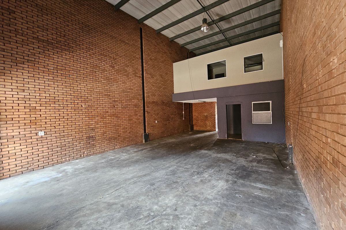 Spacious industrial warehouse unit featuring high ceilings, exposed brick walls, concrete flooring, and a functional mezzanine level for additional storage or office space.