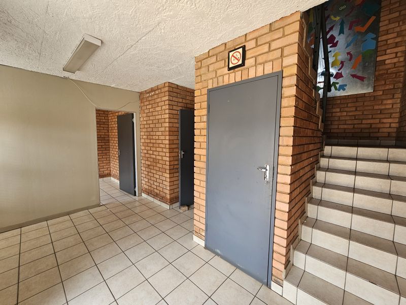 Industrial hallway featuring exposed brick walls, tiled flooring, and a staircase leading to upper levels.