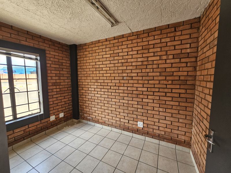 An empty office space featuring exposed brick walls, ceramic tiled flooring, and natural light through a window with security bars.