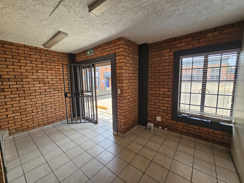 An industrial-style entry area featuring exposed brick walls, ceramic tiled flooring, and secure access points with security gates and window bars.