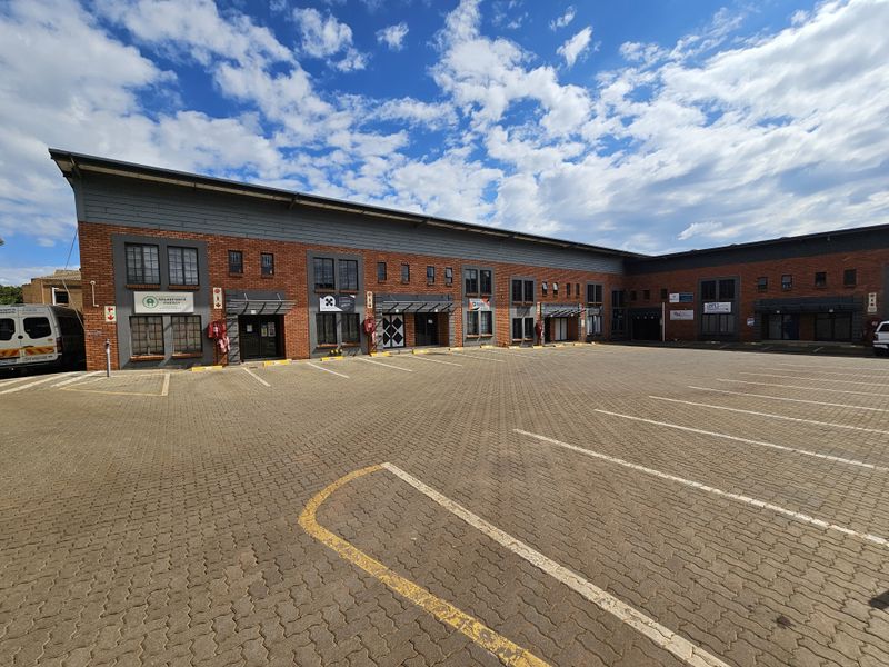 Front exterior view of an industrial office park featuring a large paved parking area and multi-unit brick facade with security features.