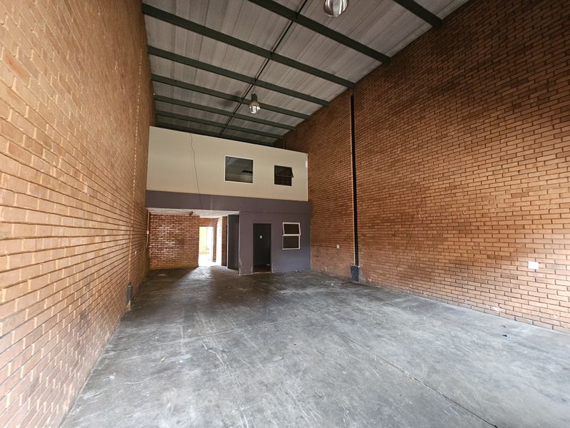 Spacious industrial warehouse unit featuring high ceilings, exposed brick walls, concrete flooring, and an integrated mezzanine level suitable for office or storage use.