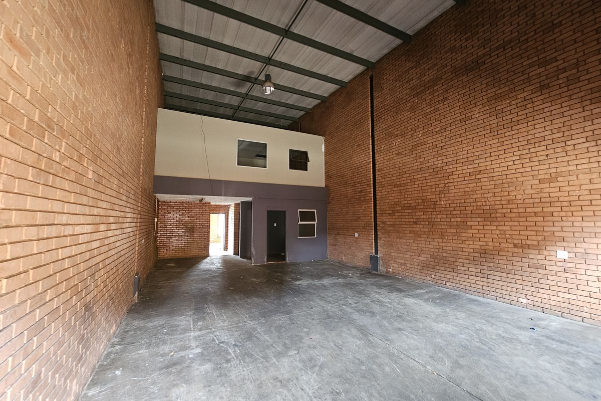 Spacious industrial warehouse unit featuring high ceilings, exposed brick walls, concrete flooring, and an integrated mezzanine level suitable for office or storage use.