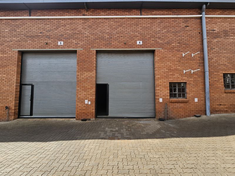 Industrial warehouse exterior featuring two large roller shutter doors, red brick facade, and paved driveway access.