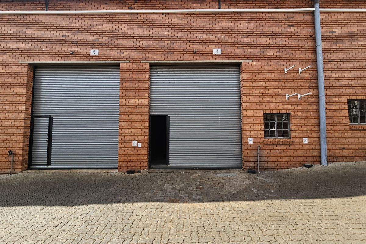 Industrial warehouse exterior featuring two large roller shutter doors, red brick facade, and paved driveway access.