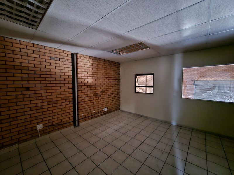 An empty office space featuring an exposed brick feature wall, ceramic tiled flooring, and a suspended ceiling with recessed lighting.