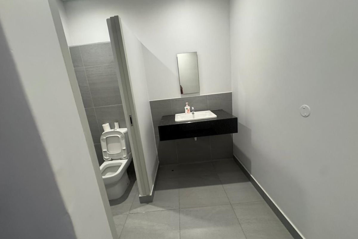 A clean, modern industrial-style restroom featuring a wall-mounted vanity with a basin, a separate toilet cubicle, and neutral grey floor and wall tiling.