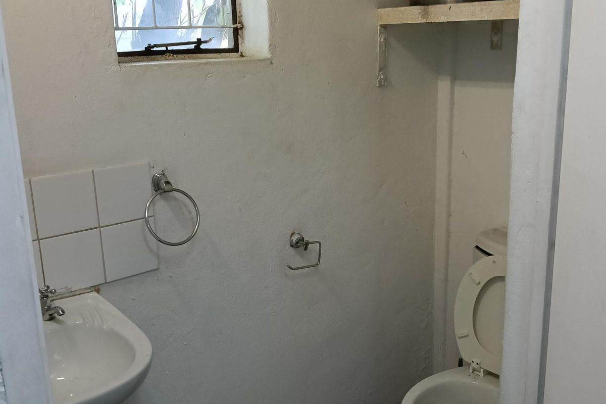 A small, functional industrial-style restroom featuring a wall-mounted basin, toilet, and overhead water storage tank.