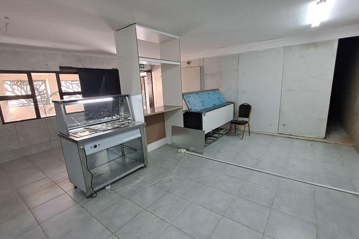 A commercial kitchen space featuring tiled flooring, a built-in service counter, and basic lighting, currently in need of cosmetic finishing and wall repairs.