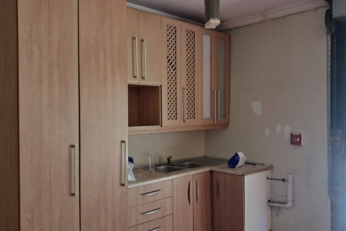 A compact kitchenette area featuring light wood-finish cabinetry, a stainless steel sink, and direct access to an outdoor area.