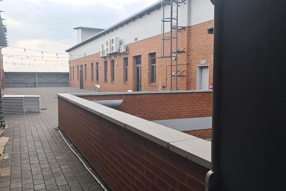 A spacious paved rear courtyard area featuring brick facade walls, external access stairs, and wall-mounted air conditioning units.