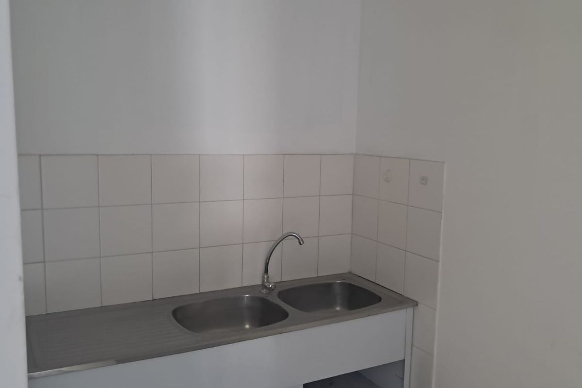 A simple, functional kitchenette area featuring a stainless steel double sink with a tiled splashback, suitable for office utility use.