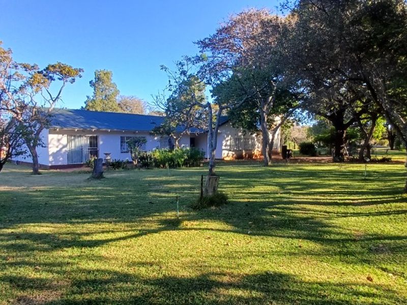 A view of the rear elevation of the property, featuring a metal roof, security bars on windows, and a spacious, tree-lined garden.