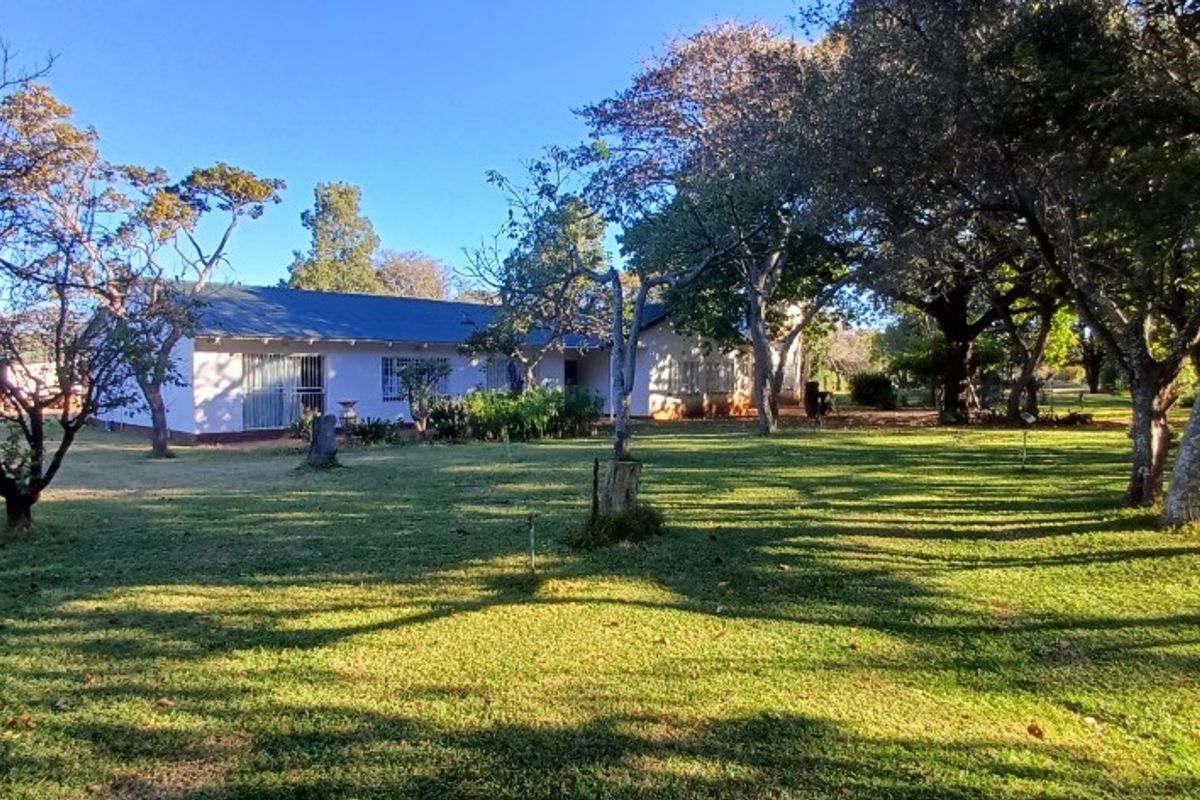A view of the rear elevation of the property, featuring a metal roof, security bars on windows, and a spacious, tree-lined garden.