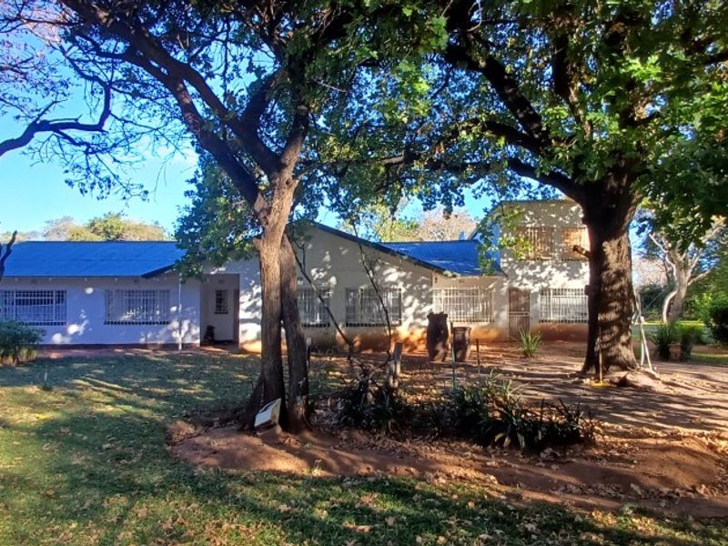 Front elevation of a single-story small holding residence featuring a metal roof, security bars, and established trees on a spacious plot.