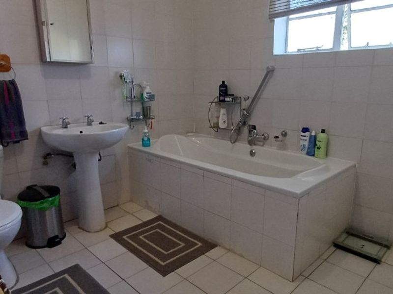 A functional bathroom featuring a pedestal basin, built-in bathtub, and toilet with neutral wall and floor tiling.