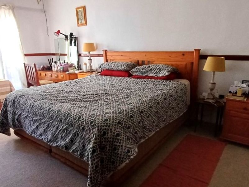 A spacious bedroom featuring neutral walls, a wooden dado rail, and carpeted flooring, offering a comfortable and functional living space.