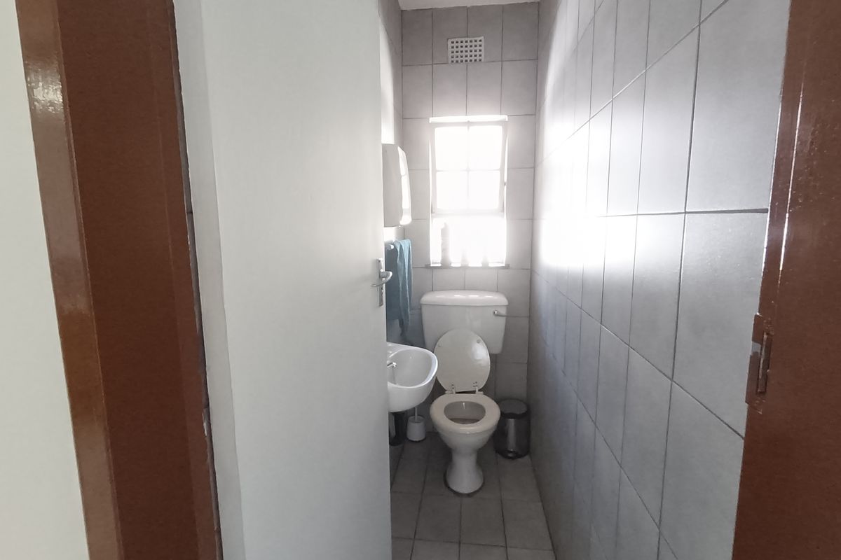 A compact bathroom featuring a standard toilet, wall-mounted basin, and full-height ceramic wall tiling.