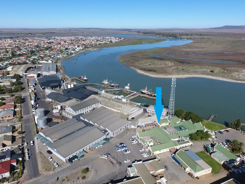 Aerial view of a commercial property complex situated along the waterfront, featuring multiple buildings with metal roofing and an adjacent parking area.