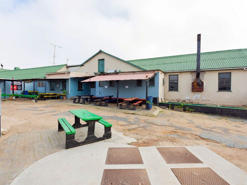 Rear exterior courtyard of a restaurant featuring a covered patio area, external chimney, and paved ground surfaces in need of maintenance.