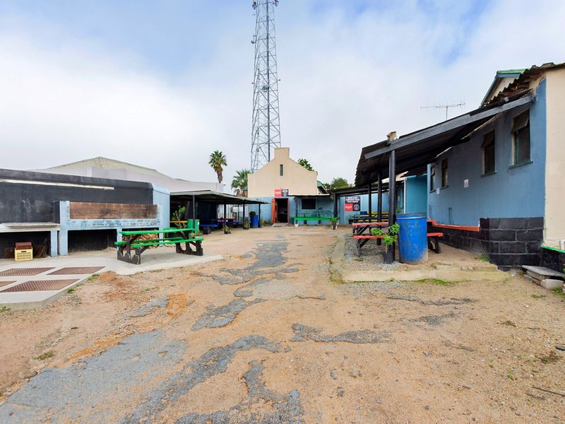 Outdoor restaurant courtyard area featuring a built-in braai, covered patio sections, and weathered asphalt paving in need of maintenance.