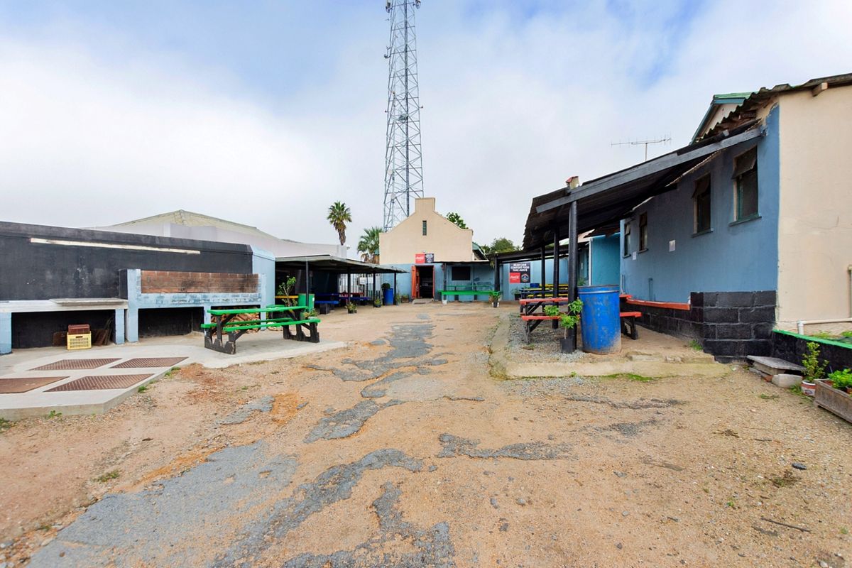 Outdoor restaurant courtyard area featuring a built-in braai, covered patio sections, and weathered asphalt paving in need of maintenance.