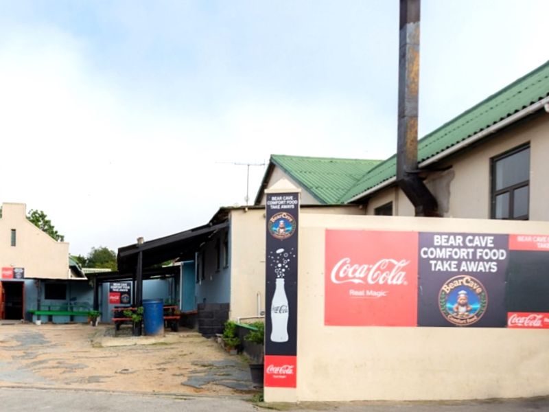 Exterior view of the restaurant entrance featuring a paved driveway, perimeter wall, and metal roofing structure.