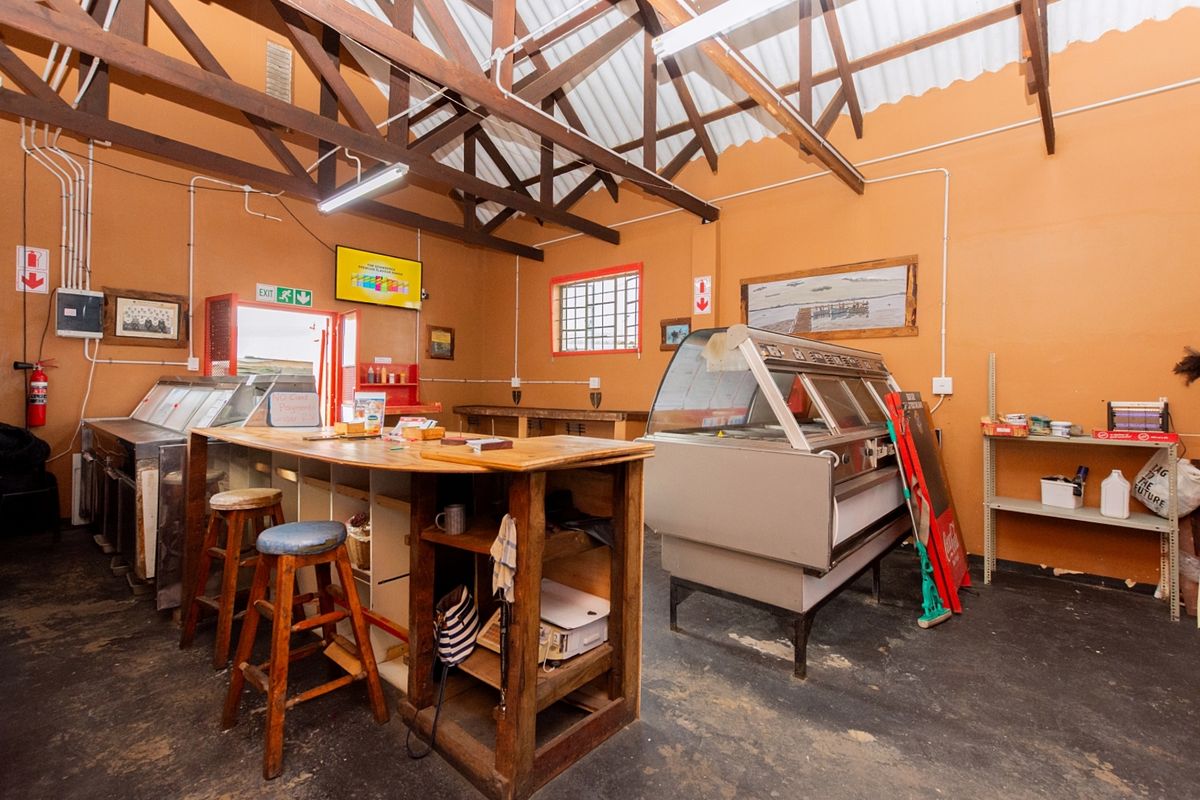 Commercial kitchen space featuring exposed timber roof trusses, refrigerated display units, and a central service counter, suitable for food service operations.