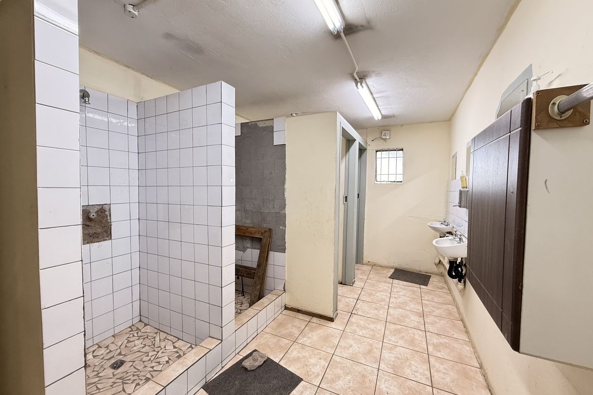 Industrial communal bathroom facility featuring tiled shower stalls, multiple wall-mounted basins, and fluorescent lighting.