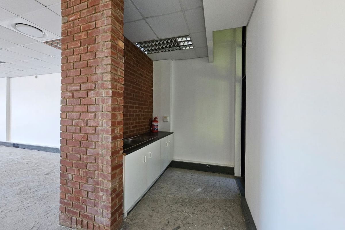 A compact kitchenette area featuring a built-in sink, white cabinetry, and an exposed brick pillar, set within an open-plan office space.