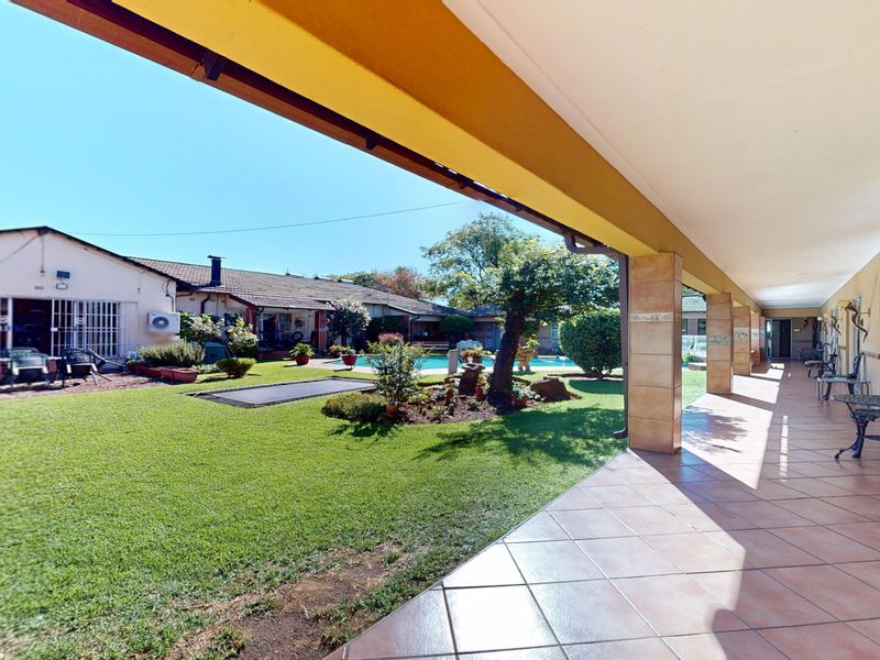 A spacious covered patio overlooking a well-maintained garden and swimming pool area, providing an ideal space for outdoor relaxation and entertainment.
