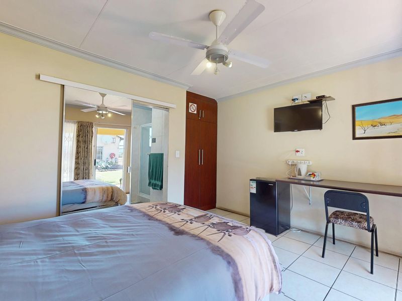 A functional bedroom featuring tiled flooring, a ceiling fan, built-in wardrobe with mirrored doors, and a wall-mounted desk area.
