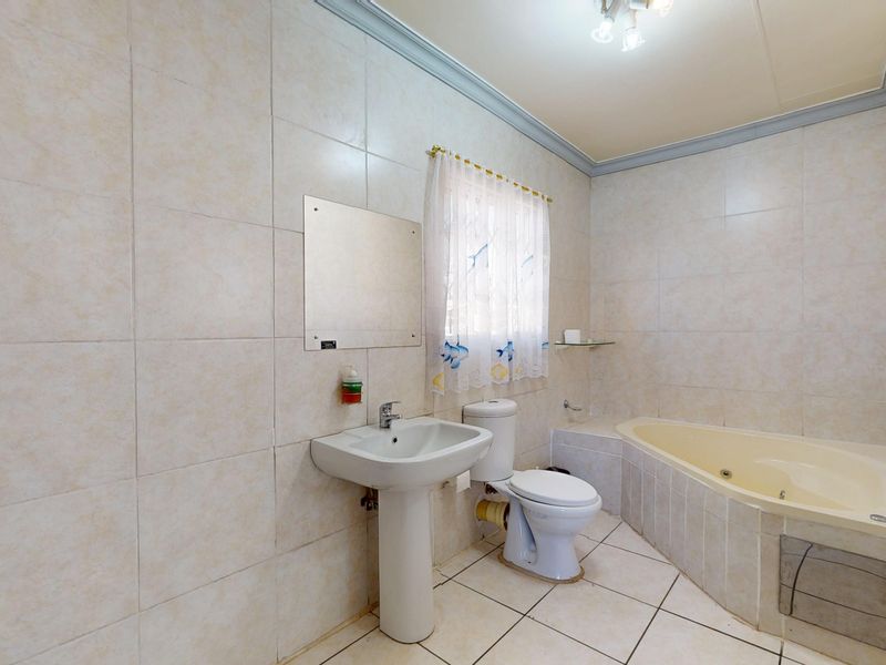 A functional bathroom featuring a pedestal basin, toilet, and a built-in bathtub with full-height wall tiling and tiled flooring.