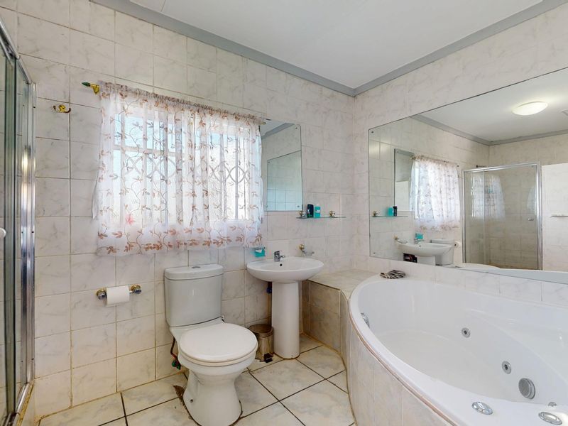 A functional bathroom featuring a corner jetted bathtub, separate shower enclosure, pedestal basin, and large wall mirror with neutral ceramic tiling.