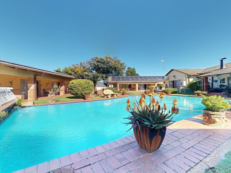 Spacious outdoor pool area featuring brick paving, surrounding covered patios, and solar panels installed on the roof of the guest house buildings.