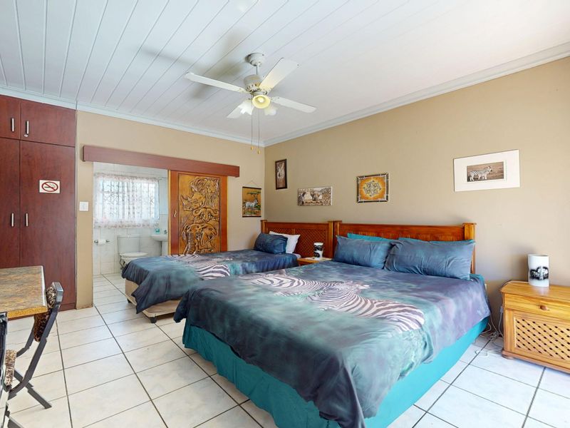 Spacious bedroom featuring tiled flooring, built-in cupboards, a ceiling fan, and direct access to an en-suite bathroom.
