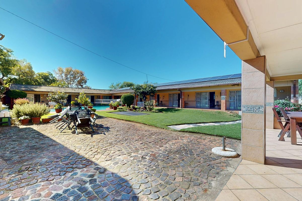 Spacious rear courtyard featuring a cobblestone patio, covered veranda, manicured lawn, and a swimming pool, set within a guest house complex.