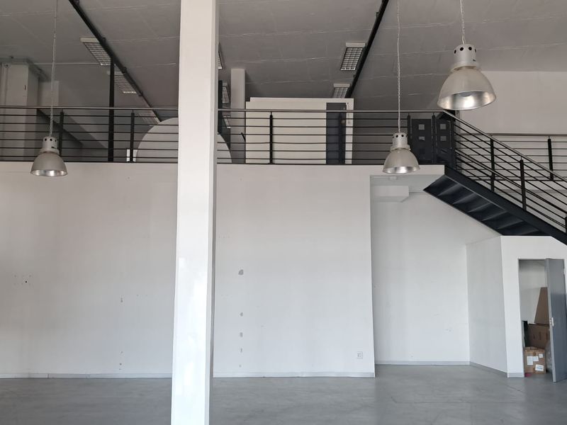 Spacious industrial open-plan unit featuring a mezzanine level, metal staircase, high ceilings with pendant lighting, and durable concrete flooring.
