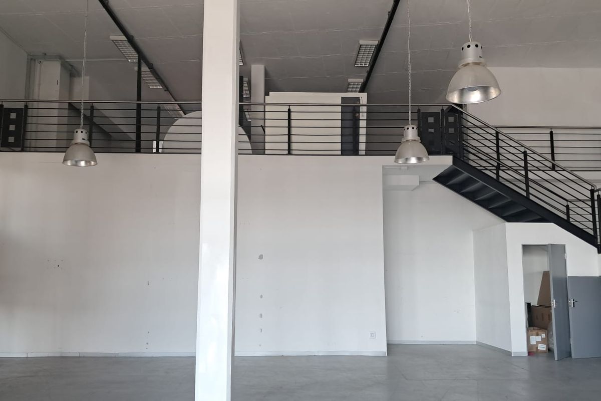 Spacious industrial open-plan unit featuring a mezzanine level, metal staircase, high ceilings with pendant lighting, and durable concrete flooring.