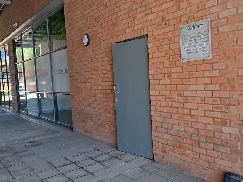Exterior view of an industrial property featuring an exposed brick facade, large glass storefront windows, and a paved walkway entrance.