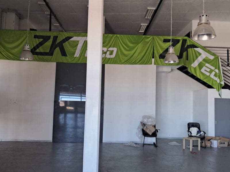 Spacious open-plan industrial unit featuring high ceilings, concrete flooring, a mezzanine level with a metal staircase, and industrial-style pendant lighting.