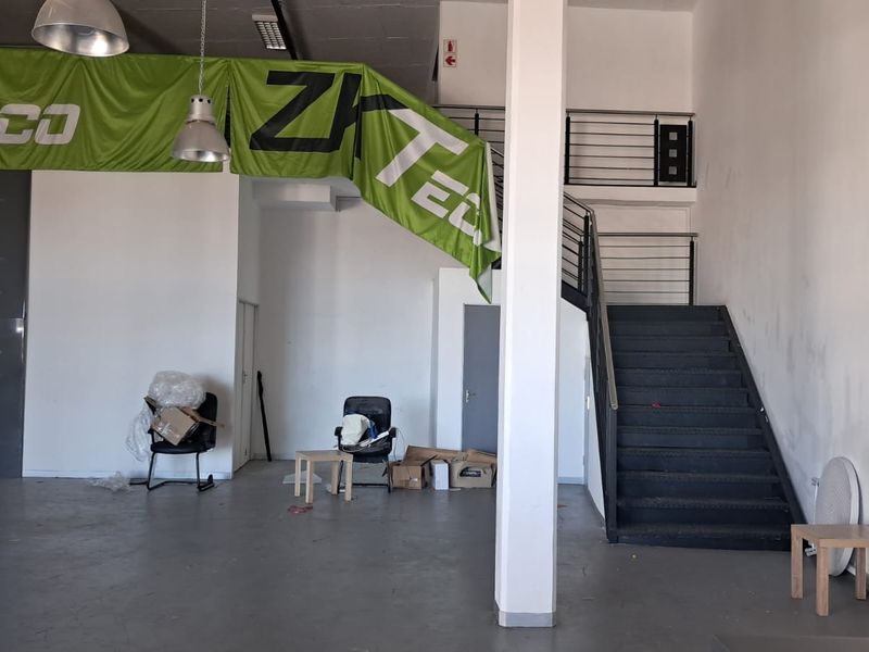 Spacious industrial open-plan area featuring concrete flooring, an internal staircase with metal railings, and high ceilings, suitable for versatile commercial or office use.