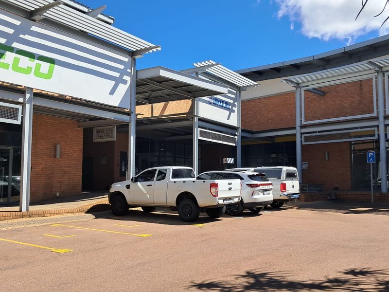 Front exterior view of a modern industrial office or retail complex featuring brick masonry, steel structural elements, and a paved parking area.