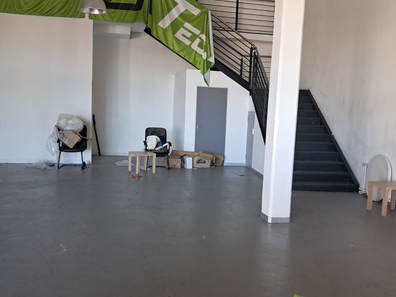 Open plan industrial space featuring concrete flooring, a central support column, and a metal staircase leading to an upper level.