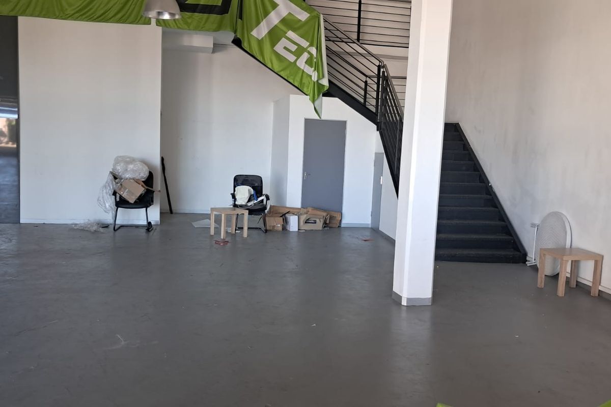 Open plan industrial space featuring concrete flooring, a central support column, and a metal staircase leading to an upper level.