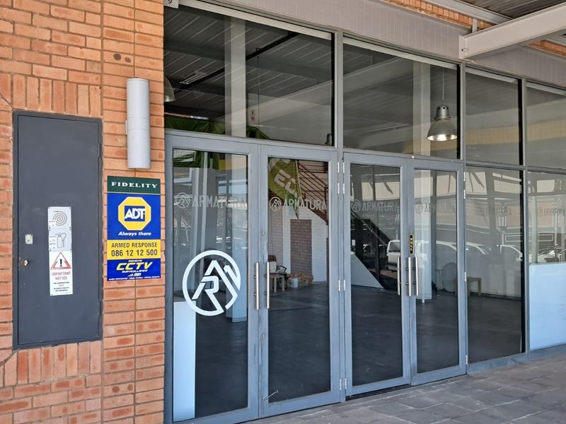 Industrial property entrance featuring a brick facade and large aluminium-framed glass doors with security signage.