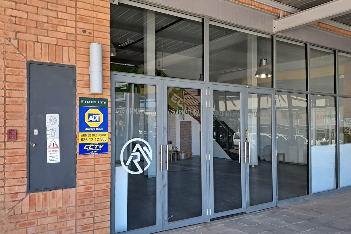 Industrial property entrance featuring a brick facade and large aluminium-framed glass doors with security signage.